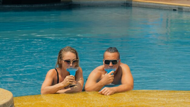 Para przytula się i całuje pijąc niebieski alkohol koktajlowy w basenie w hotelu na świeżym powietrzu
