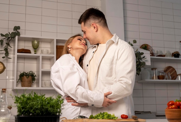 Para przytulająca się i uśmiechająca się w kuchni podczas gotowania przystojnego mężczyzny i pięknej kobiety patrzących na siebie