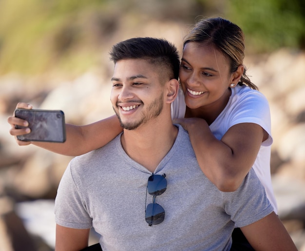 Para selfie na świeżym powietrzu i uścisk z opieką uśmiechu lub miłością przez niewyraźne tło w słońcu Mężczyzna czarna kobieta i smartfon do cyfrowego obrazu ze szczęściem do mediów społecznościowych podczas wędrówki