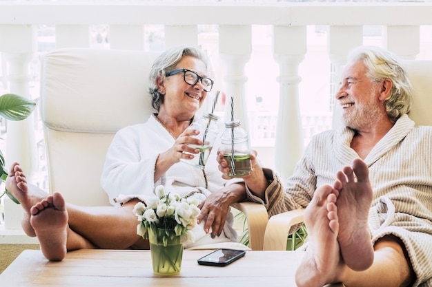 Para seniorów lub dojrzałych ludzi w spa w hotelu lub domu brzęcząca koktajlem lub napojem - bawi się z nogami na stole patrząc między sobą