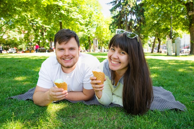 Para siedząca na koce i jedząca lody w miejskim parku w letni dzień