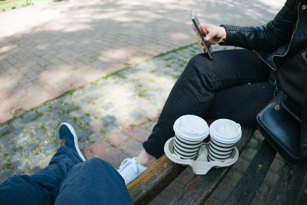 Para siedzi na ławce w parku miejskim pijąc kawę