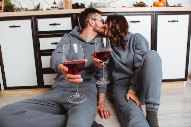 Para siedzi na podłodze kuchnia pije wino w szklankach całuje, girlandy domu przytulne wnętrze