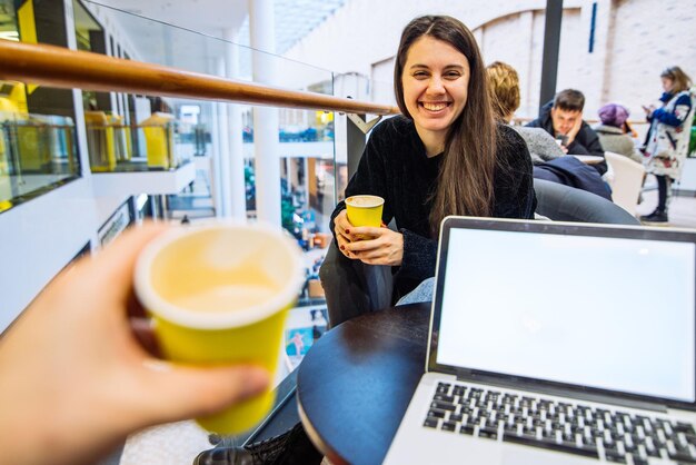 Para siedzi w kawiarni, pije kawę w żółtych filiżankach, mężczyzna pracuje na laptopie, podczas gdy kobieta sprawdza miejsce na kopię telefonu