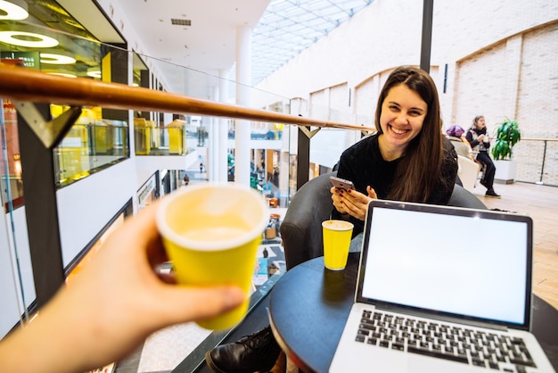 Para siedzi w kawiarni, pije kawę w żółtych filiżankach, mężczyzna pracuje na laptopie, podczas gdy kobieta sprawdza miejsce na kopię telefonu