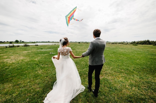 Para ślubna biegająca z powrotem po boisku, pozwalająca latać latawiec, bawić się i trzymać latawiec.
