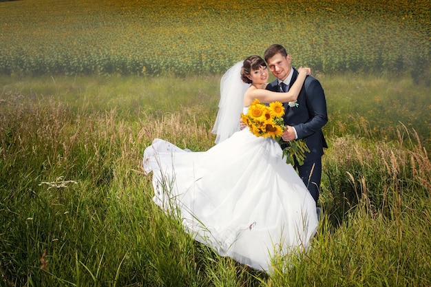 Para ślubna w letnim polu z bukietem słoneczników