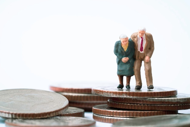 Zdjęcie para starszych emerytów miniaturowa postać stojąca na szczycie układania monet dla bogactwa planowania finansowego oszczędzania pieniędzy i ubezpieczenia na życie koncepcji emerytalnej