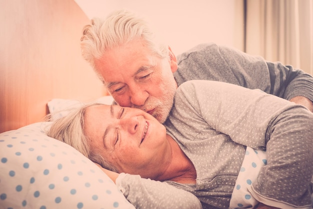 Para starszych kaukaskich mężczyzn i kobiet całujących się wczesnym rankiem w łóżku w domu dla miłości codziennie bez limitu wieku - koncepcja na zawsze razem dla szczęśliwych wesołych ludzi poślubionych w związku