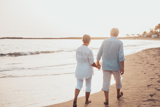 Para starych, dojrzałych ludzi chodzących razem po piasku i bawiących się na piasku plaży, ciesząc się chwilą i przeżywając ją Dwóch uroczych zakochanych seniorów ma funxA