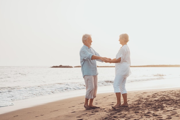 Para starych dojrzałych ludzi tańczy razem i bawi się na piasku na plaży, ciesząc się chwilą i przeżywając ją Portret zakochanych seniorów patrzących na siebie