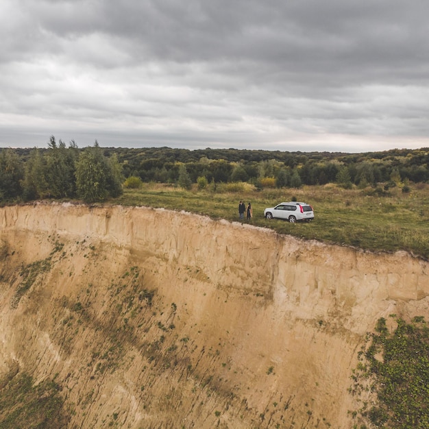 Para stojąca na klifie w pochmurną pogodę w pobliżu białego suv