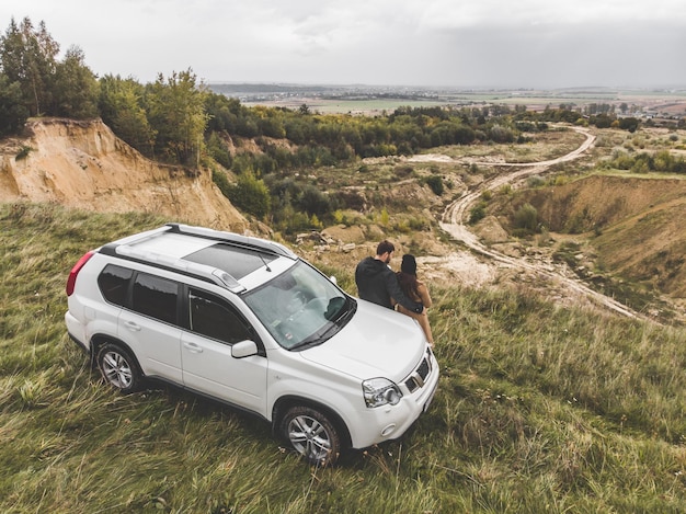 Para stojąca w pobliżu samochodu suv na klifie z pięknym widokiem z góry