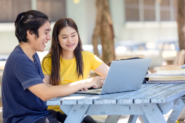 Para studentów siedzi i korzysta z laptopa na uniwersytecie na świeżym powietrzu, przeprowadzając badania online