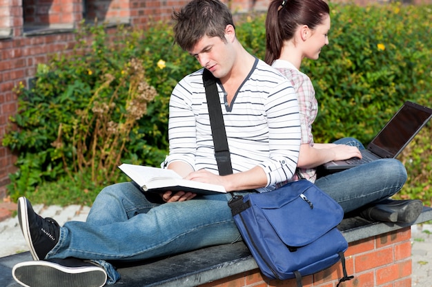 Para studentów za pomocą laptopa i czytając książkę siedzi