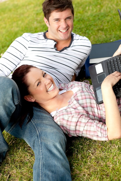 Para szczęśliwi ucznie używa laptopu lying on the beach na trawie