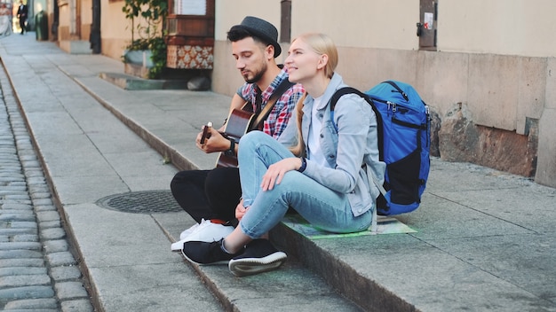 Para turystów siedzi na chodniku, gra na gitarze i odpoczywa. Zwiedzanie pięknego europejskiego miasta.