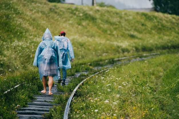 Para turystów w płaszczach przeciwdeszczowych spaceruje po linii kolejowej