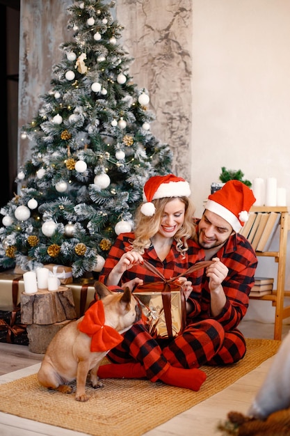 Para Ubrana W świąteczną Czerwoną Piżamę W Kratę Siedzi Na Podłodze Z Psem