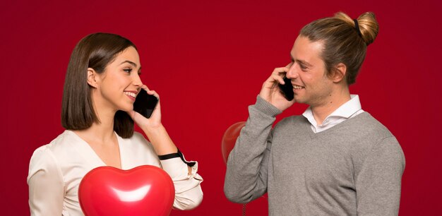 Para utrzymuje rozmowę z telefonem komórkowym nad czerwonym tłem w walentynki
