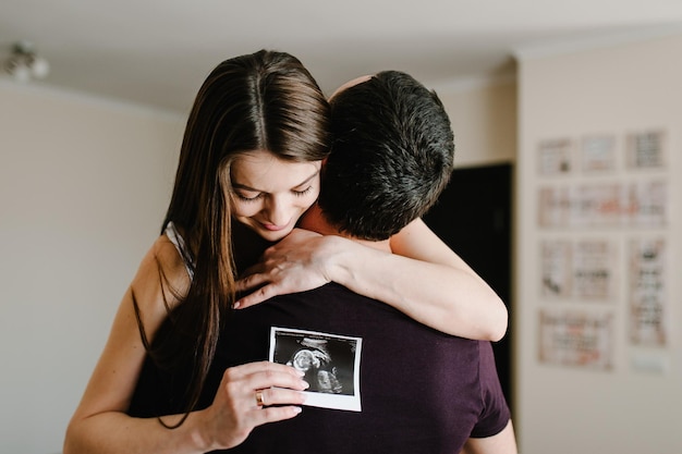 Para w ciąży trzymająca się na rękach USG dziecka Mąż mężczyzna przytulający ciężarną żonę w domu Szczęśliwa rodzina oczekiwanie ciąży Czarno-białe zdjęcie
