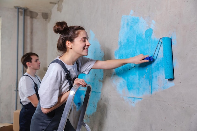 Zdjęcie para w nowym domu podczas prac remontowych wspólne malowanie ścian szczęśliwa rodzina trzymająca wałek malarski malowanie ścian niebieską farbą w nowym domu renowacja domu diy odnów koncepcję domu