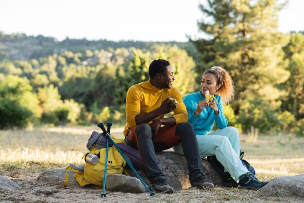 Para w przyrodzie obiad po wędrówce jedzą owoce siedząc na skale przy zachodzie słońca podczas rozmowy