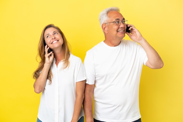 Para w średnim wieku na żółtym tle rozmawia z telefonem komórkowym