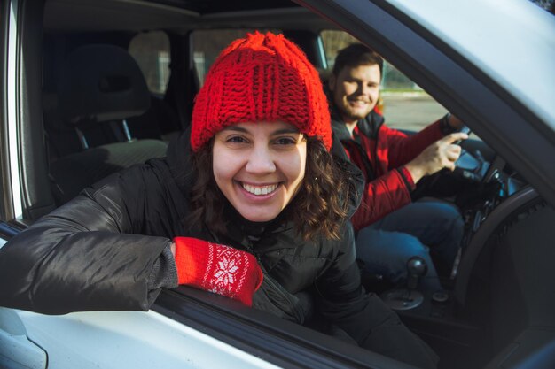 Para w wynajętym samochodzie uśmiechnięta kobieta w czerwonym kapeluszu zimowym