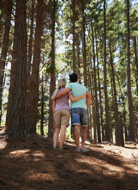 Para wędruje i przytula się w lesie z miłości, uściska lub wspiera w zaufaniu, opiece lub wiązaniu w przyrodzie, widok z tyłu lub z tyłu młodego mężczyzny i kobiety w romantycznym uczuciu lub spaceru razem w lesie na świeżym powietrzu.