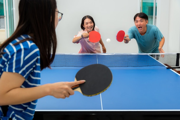 Para Zabawy Grając W Tenisa Stołowego Lub Ping Ponga W Pomieszczeniach Razem Z Rekreacją Z Rywalizacją W Grach Sportowych W Domu. Ojciec, Matka I Córka Azjatycka Rodzina Spędza Czas Na Rekreacji W Domu W Tajlandii