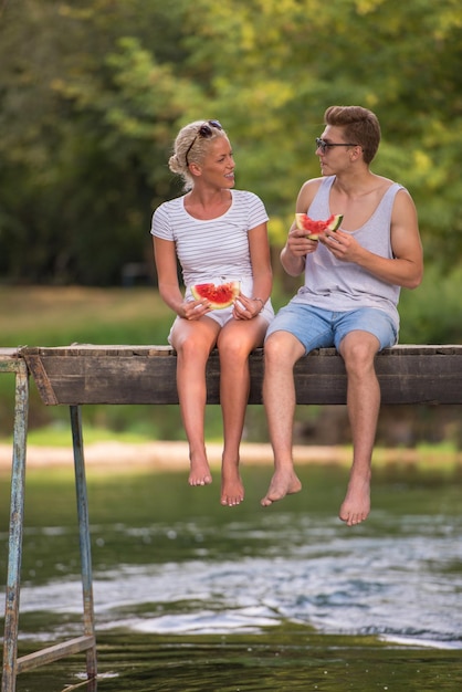 para zakochanych, ciesząc się arbuzem, siedząc na drewnianym moście nad rzeką w pięknej przyrody