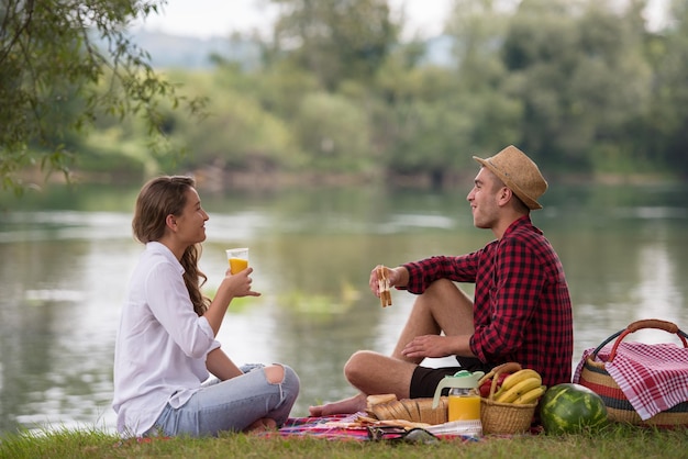 Para zakochanych, ciesząc się piciem i jedzeniem w czasie pikniku w pięknej przyrody na brzegu rzeki