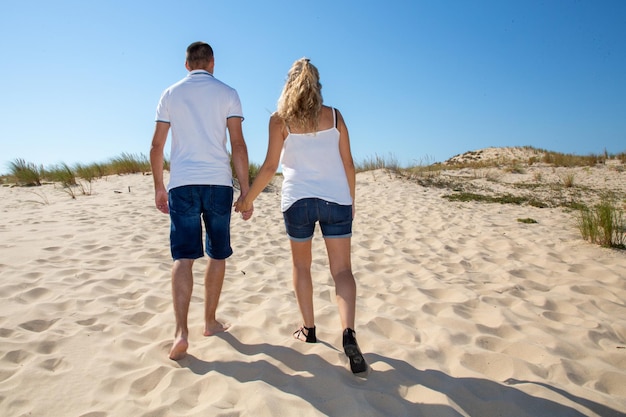 Para zakochanych młodych spacerów trzymających się za ręce na wydmach na plaży w letnie wakacje