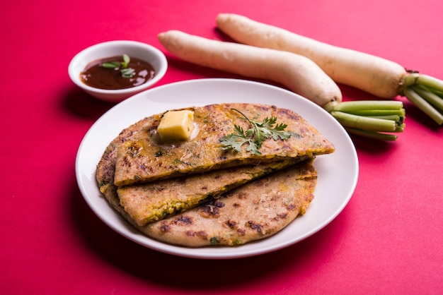 Zdjęcie paratha nadziewana daikon, rzodkiew lub mooli, podana na talerzu z masłem i keczupem pomidorowym, na kolorowym lub drewnianym tle. selektywne skupienie