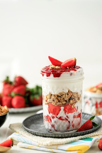 Parfait jogurtowo-truskawkowy z miętą muesli i świeżymi jagodami w szklanym słoiku na białym drewnianym stole Koncepcja zdrowego śniadania