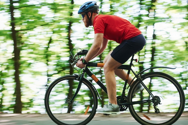 Park naturalny. Rowerzysta na rowerze jest na asfaltowej drodze w lesie w słoneczny dzień