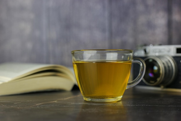 Parzona zielona herbata ziołowa w przezroczystym kubku w pobliżu otwartej książki i zabytkowej kamery na ciemnym tle