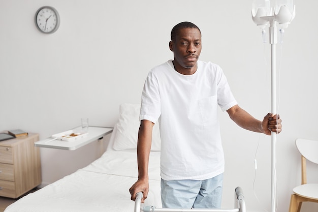 Pas w górę portret afroamerykańskiego mężczyzny w szpitalu, trzymającego stojak kroplówki iv i patrząc na kamerę, kopia przestrzeń