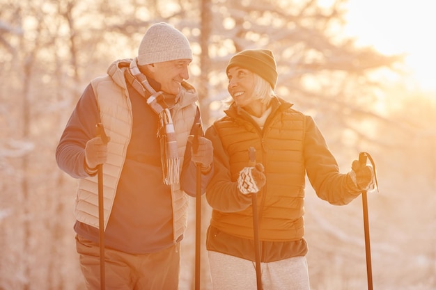 Pas w górę portret aktywnej pary seniorów cieszącej się nordic walk z kijkami w pięknym zimowym lesie