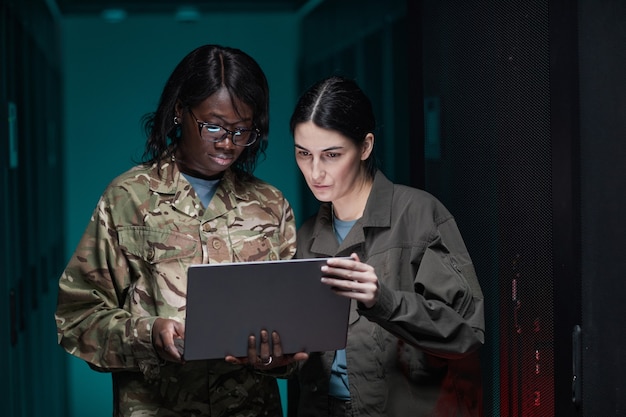 Pas w górę portret dwóch młodych kobiet w wojskowym mundurze, przy użyciu laptopa stojąc w serwerowni, kopia przestrzeń