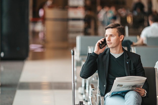 Pasażer w poczekalni na lotnisku czeka na samolot samolotowy, młody mężczyzna ze smartfonem na lotnisku czekaj