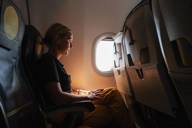 Pasażerka leci samolotem Dziewczyna siedzi w samolocie i wygląda przez okno, jadąc w podróż