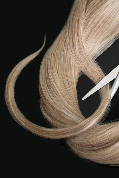 Pasmo blond włosów nożyczkami na czarnym tle Zbliżenie
