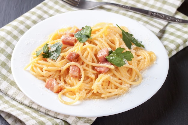 Pasta Carbonara z szynką i serem na ręczniku w kratkę.