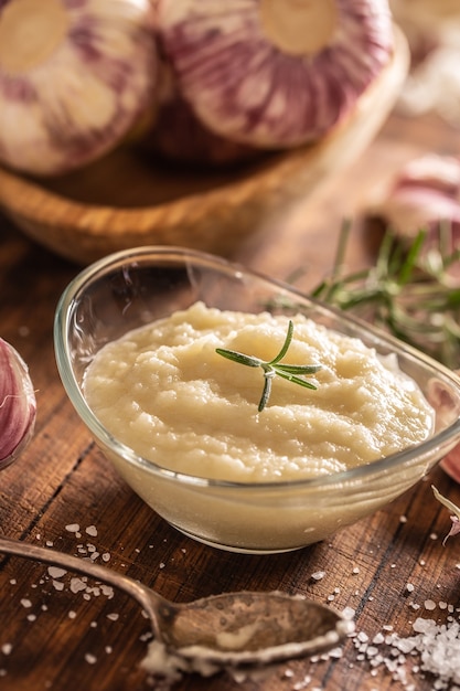 Pasta czosnkowa w szklanej misce z obranym czosnkiem, solą i główkami czosnku.