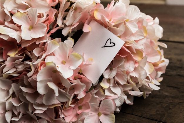 Pastelowe różowe kwiaty hortensji i kartka papieru na drewnie. miejsce na tekst