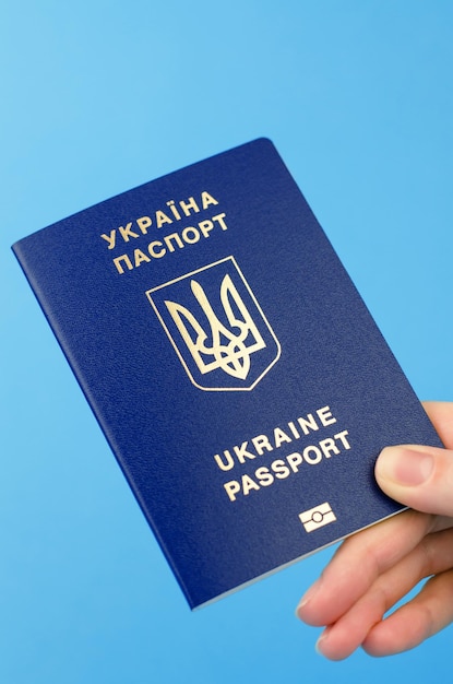 Paszport obywatela Ukrainy w kobiecej dłoni na niebieskim tle zbliżenie Napis w języku ukraińskim Paszport Ukrainy