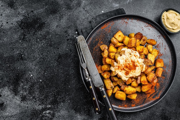 Patatas Bravas, tradycyjne hiszpańskie tapas, pieczony ziemniak z pikantnym sosem pomidorowym. Czarne tło. Widok z góry. Skopiuj miejsce.