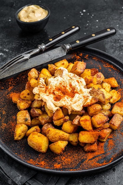 Zdjęcie patatas bravas, tradycyjne hiszpańskie tapas, pieczony ziemniak z pikantnym sosem pomidorowym. czarne tło. widok z góry.